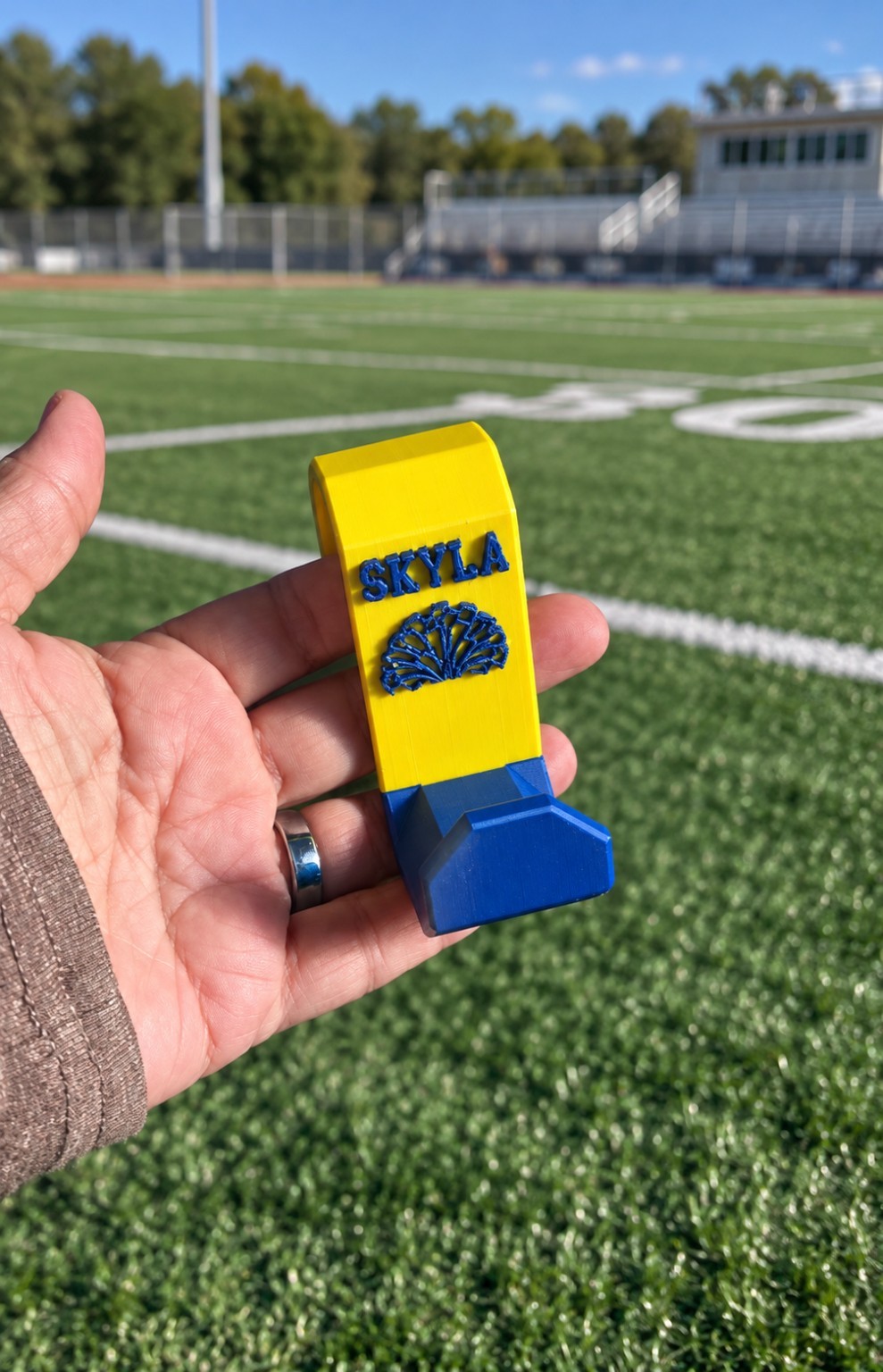 Personalized yellow and blue Sports Bag Fence Hook with SKYLA lettering, held beside a sports field
